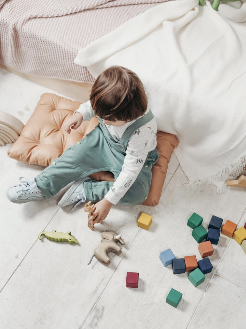 A child in overalls playing with colourful wooden blocks on the floor